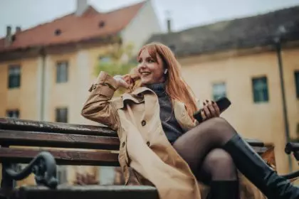 A happy chic lady sitting on a bench on street and enjoying music.