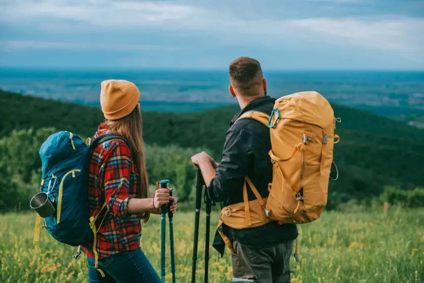 Couple of hikers using trekking poles and wearing backpacks with camping gear