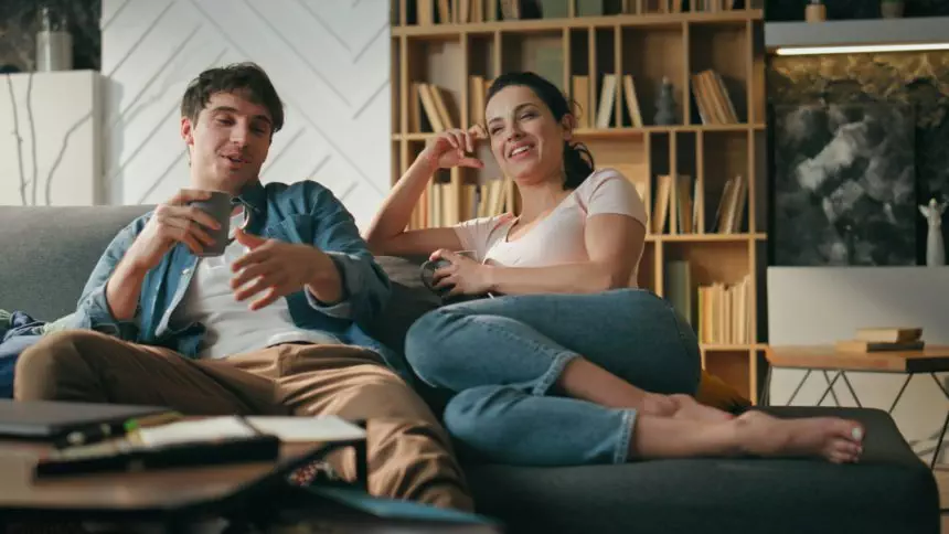 Smiling pair talking couch holding cups coffee. Couple relaxing family evening