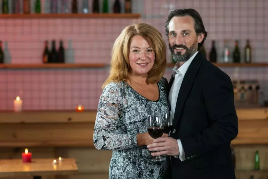 Waist up portrait of excited adult loving couple celebrating special occasion with red wine