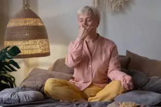 Senior woman practicing yoga at home, making Alternate Nostril Breathing exercise