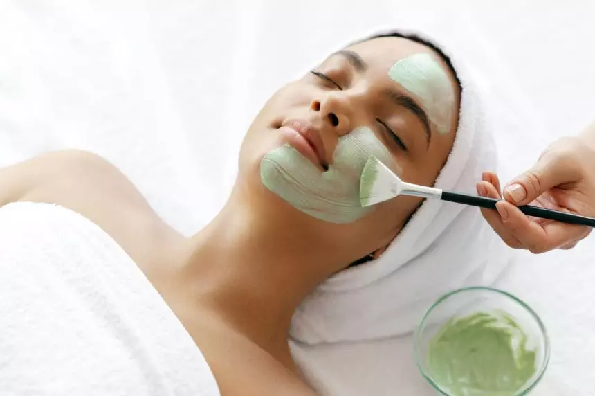 Top view of beauty procedure, therapist applying green face mask on the face of a beautiful