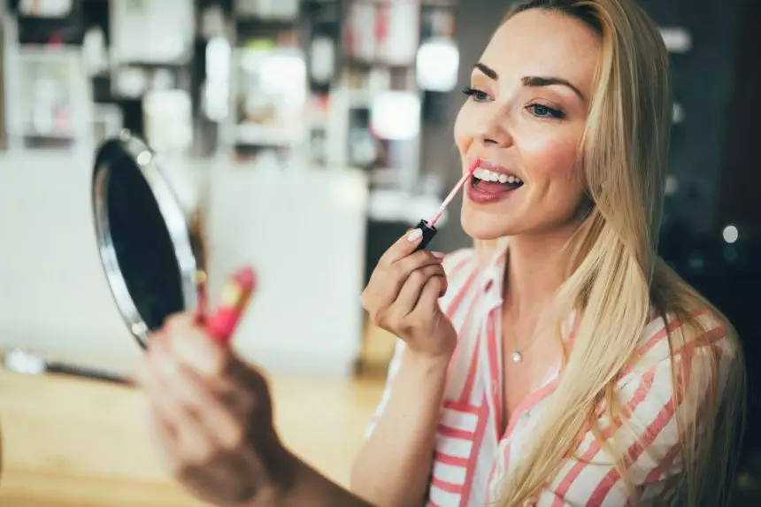 Beautiful young woman applying lips makeup