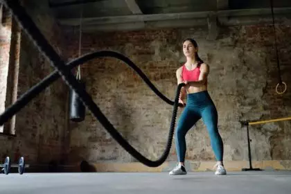 Young woman exercising with battle ropes at the gym. Strong female athlete doing crossfit workout