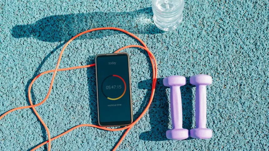 Smartphone with workout mobile app, skipping rope, dumbbells and water bottle on outdoor sports