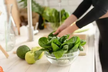 Preparing healthy foods. Woman in sport clothes washing spinach in the kitchen